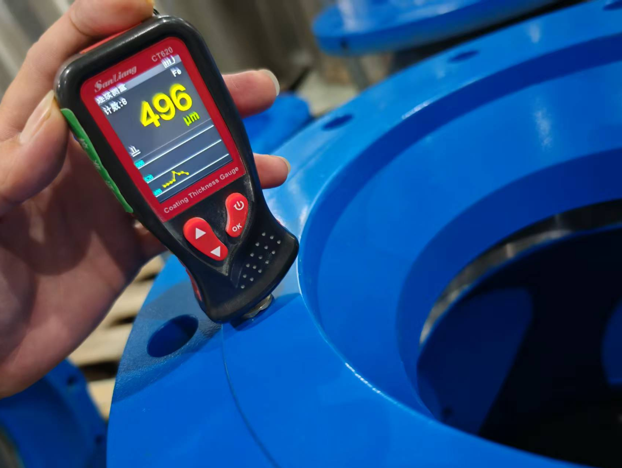 Digital coating thickness gauge reading 496 µm on blue epoxy FBE coating of a large water valve during J-VALVES factory QC inspection